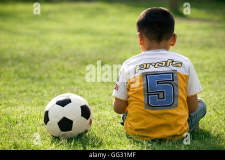 Ragazzo seduto con un calcio sul suo fianco Foto Stock