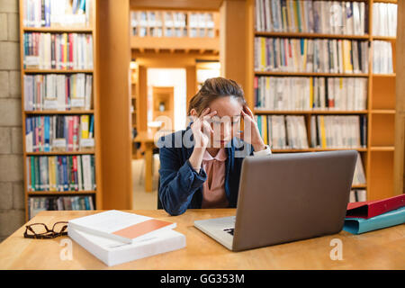 Teso giovane donna utilizzando laptop in biblioteca Foto Stock