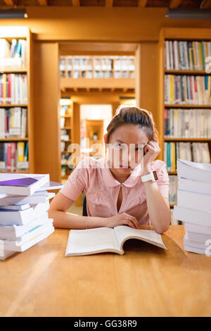 Teso giovane donna studiare in biblioteca Foto Stock