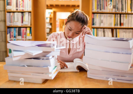 Teso giovane donna studiare in biblioteca Foto Stock