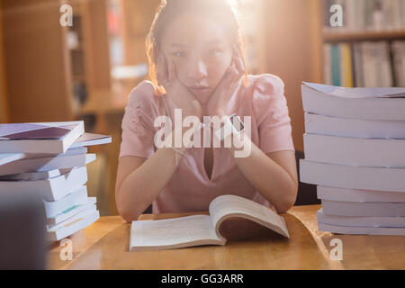 Triste giovane donna studiare in biblioteca Foto Stock