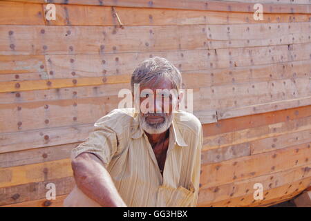 Ritratto di un Gujarati uomo seduto davanti a un tradizionale dhow di legno in Mandvi, Gujarat, India Foto Stock