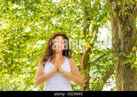 Donna attraente pregando con mani giunte per benedizioni Foto Stock