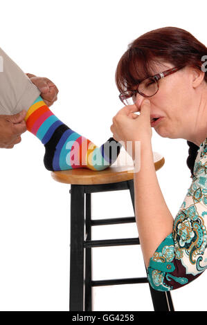 Una donna discusso tenendo il suo naso chiuso dall'odore di suo marito calzini, isolato per sfondo bianco. Foto Stock