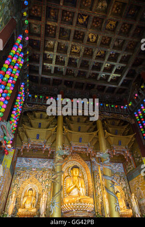 Tall Dharma Hall, tetto ornato e tre Golden Statue di Buddha all'interno Yakchunsa (Yakcheonsa) tempio su Jeju Island, la Corea del Sud. Foto Stock