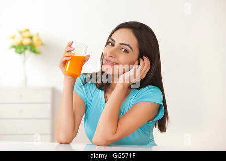 Ritratto di giovane e bella donna di bere succo di arancia a casa Foto Stock