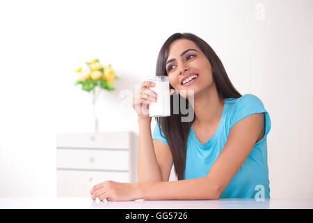 Felice giovane donna tenendo un bicchiere di latte a casa Foto Stock