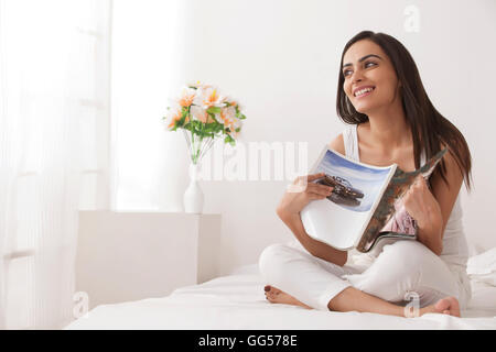 Lunghezza completa di felice giovane donna rivista di contenimento sul letto Foto Stock