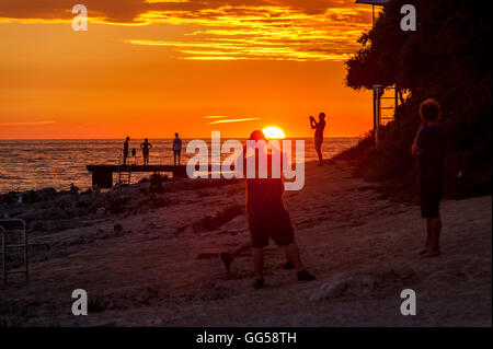 Le persone in piedi in una serata beaching guardare il tramonto, scattare foto e godersi il momento. Foto Stock