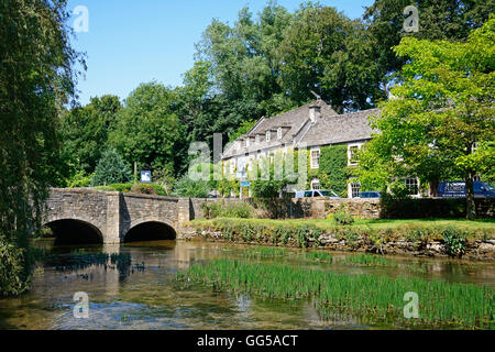 Vista lungo il Fiume Coln verso il ponte di pietra con la Swan Hotel verso la parte posteriore, Bibury, Cotswolds, Gloucestershire, Inghilterra, Foto Stock