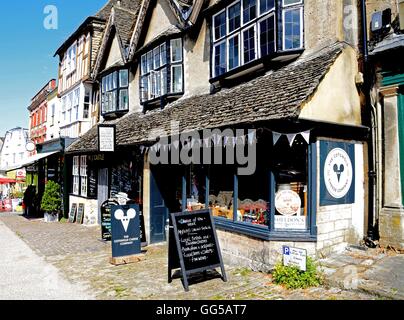 Negozi lungo la collina via commerciale con negozio di formaggio in primo piano, burford, Oxfordshire, Inghilterra, Regno Unito, Europa occidentale. Foto Stock