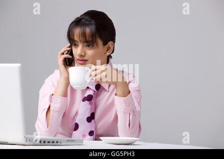 Imprenditrice di bere il caffè mentre si utilizza il telefono cellulare e il computer portatile Foto Stock