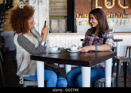 Giovane donna di scattare una foto della sua amica con lo smartphone al cafe Foto Stock