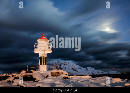 Faro e luna piena nella notte artica con il villaggio di Reine in background, Nordland, Isole Lofoten in Norvegia Foto Stock