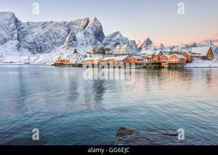 I colori dell'alba telaio le case di pescatori circondato da vette innevate, Sakrisoy nei, la Reine, Nordland, Isole Lofoten in Norvegia Foto Stock