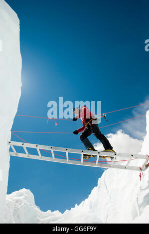 Un scalatore fa il suo modo attraverso un crepaccio utilizzando una scala provvisoria, regione di Khumbu, Himalaya, Nepal, Asia Foto Stock