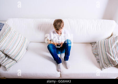 Piccolo Ragazzo seduto sul divano, giocando con lo smartphone Foto Stock