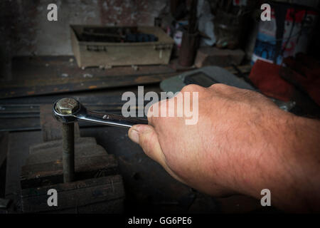 Lavoratore mano serrando o allentando il dado di un bullone arrugginito con una chiave nella vecchia bottega Foto Stock
