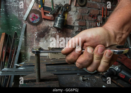 Lavoratore mano serrando o allentando il dado di un bullone arrugginito con una chiave nella vecchia bottega Foto Stock
