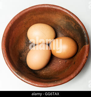 Tre uova in una ciotola di ceramica rossa su uno sfondo bianco Foto Stock