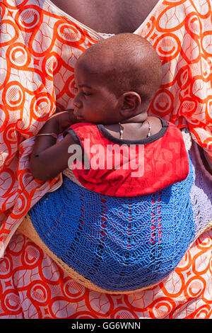 African bedik donna di trasportare un bambino mentre si fanno i lavori domestici, Ziguinchor, Casamance, Senegal Africa Foto Stock