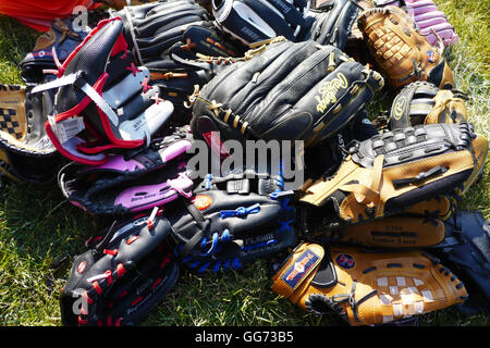 Pile di ben utilizzato guanti da baseball per bambini e adulti impilate su erba in sun. Foto Stock