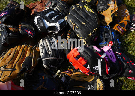 Pile di ben utilizzato guanti da baseball per bambini e adulti impilate su erba in sun. Foto Stock