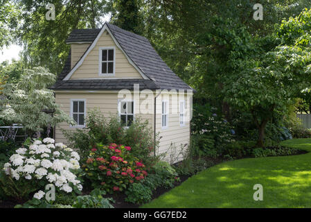 Un affascinante playhouse cottage si trova in corrispondenza del bordo di un ombreggiato giardino perenni. Foto Stock