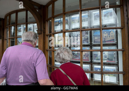 Coppia senior cercando in agenti immobiliari finestra alla proprietà in vendita in Cotswolds in Inghilterra, Regno Unito Foto Stock