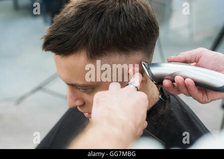 Styling professionale. Close up vista laterale del giovane uomo getting haircut dal parrucchiere con rasoio elettrico al barbiere Foto Stock