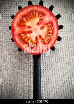 Metà pomodoro su una dentatura cucchiaio da cucina su una massa di colore grigio. L'immagine verticale. Foto Stock