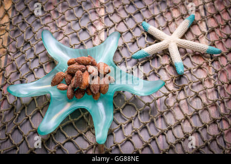 Le mandorle in una stella di mare piatto sagomato su una rete e stagionato superficie di legno Foto Stock