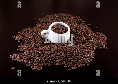 Coppa piena di chicchi di caffè al buio su un sfondo di legno Foto Stock