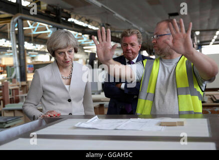 Il primo ministro Theresa Maggio con Martek Managing Director Derek Galloway (centro) parla di un lavoratore durante una visita a Martek falegnameria costruttori in New Addington, Surrey. Foto Stock