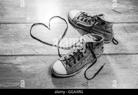 Usato, sporco sneakers, con a forma di cuore ad lacci delle scarpe su un pavimento di legno. Foto Stock