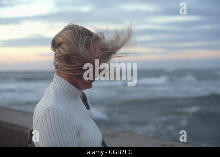Donna capelli soffiando nel vento nella parte anteriore delle onde del mare e cielo nuvoloso al tramonto Foto Stock