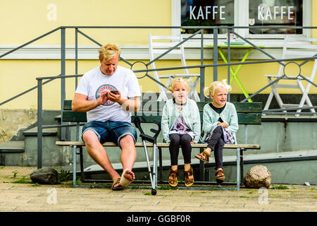 Ystad, Svezia - 1 Agosto 2016: persone reali nella vita di tutti i giorni. Uomo adulto con le stampelle e un piede male sedersi accanto a due bella ragazza Foto Stock