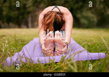 Giovane donna che fa yoga all'aperto su erba, pratica paschimottanasana posa. donna in forma seduta seduta in avanti piegata in posa durante il trai Foto Stock