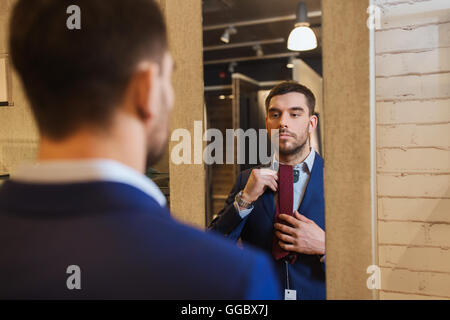 Uomo cerca sul tirante in corrispondenza dello specchio nel negozio di abbigliamento Foto Stock