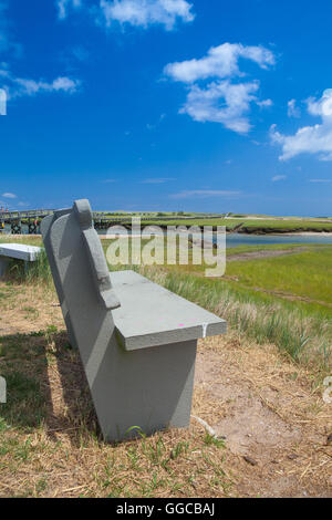 Banco di cemento vicino alla passerella per le dune. Passerella in legno si estende su una palude verso il lontano dalle dune e oceano nel Sandwi Foto Stock