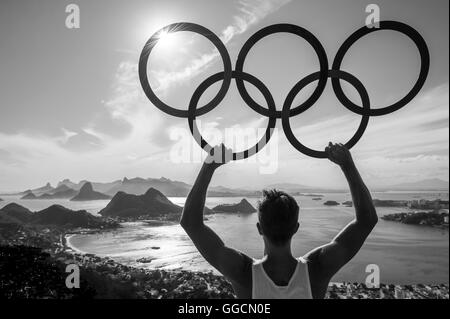 RIO DE JANEIRO - Febbraio 26, 2016: atleta sorge in silhouette monocromatiche holding anelli olimpici al di sopra di una skyline vista città. Foto Stock