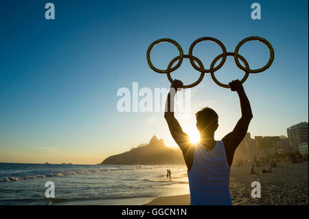 RIO DE JANEIRO - MARZO 05, 2016: atleta detiene anelli olimpici sopra tramonto vista dello skyline della citta' di due fratelli di montagna a Ipanema Foto Stock