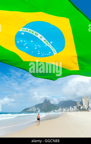 Bandiera brasiliana battenti nel sole luminoso al di sopra dello skyline della citta' presso la spiaggia di Ipanema a Rio de Janeiro in Brasile Foto Stock