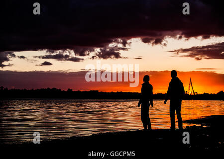 Felice l'uomo e la donna giovane a piedi e tenendo le mani su una spiaggia con un luminoso colorato sunrise sullo sfondo, coppia romantica in ama camminare al tramonto, donna e uomo in amore camminando mano nella mano Foto Stock