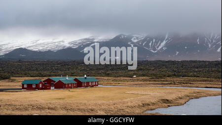 Cottage di legno case nei pressi di un piccolo lago sotto le montagne coperte di neve in Islanda Foto Stock