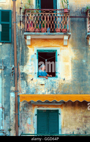 Corfù, Grecia - luglio 6, 2011: uomo vecchio nella finestra di antica casa tipica Foto Stock
