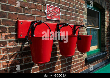 Rosso fuoco cestelli appesi a ganci in una fila di tre, in corrispondenza di un vecchio 1940's stazione ferroviaria platform Foto Stock