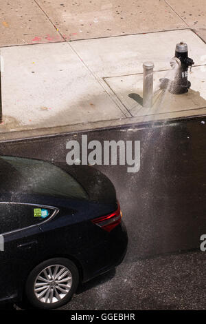 Di colore scuro Toyota automobile guida attraverso i flussi di acqua da un fuoco aperto idrante con un ugello di spruzzo attaccato Foto Stock