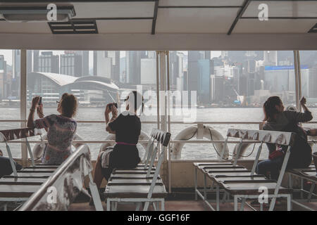 Turistica prendendo le foto con i loro telefoni cellulari sul traghetto Star di Hong Kong Foto Stock