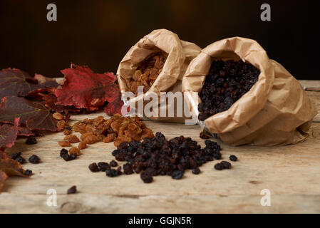 Golden e uva passa nera in sacchi di carta su un tavolo di legno Foto Stock